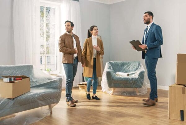 Rental Property Insurance - A Professional Real Estate Agent Shows a Spacious Bright Apartment with Big Windows to a Young Couple